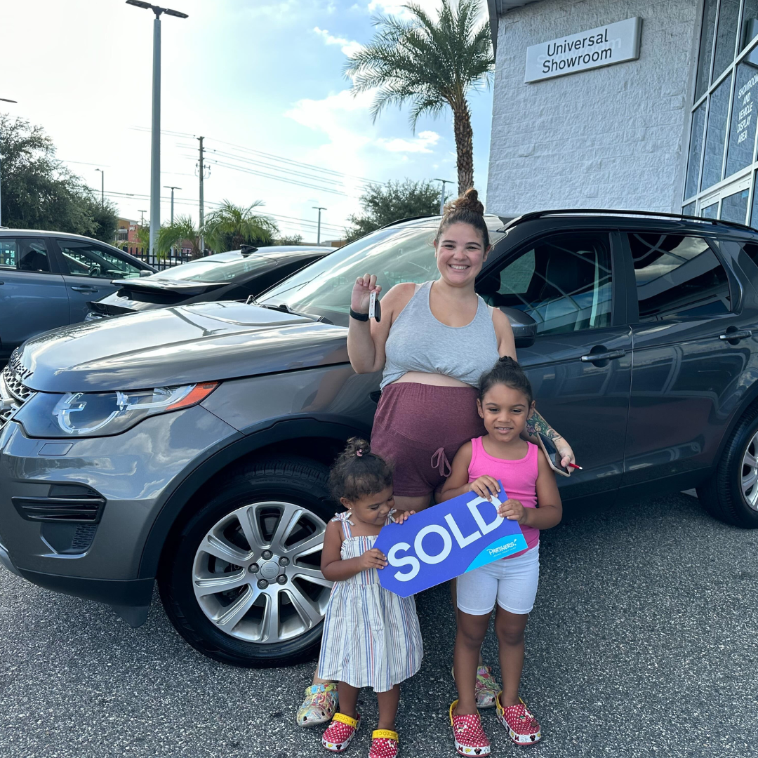 Mother holding keys in front of vehicle with her daughters